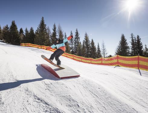 Snowboarder springt über Rampe auf Piste in Bad Kleinkirchheim Snowboarder in Bad Kleinkirchheim